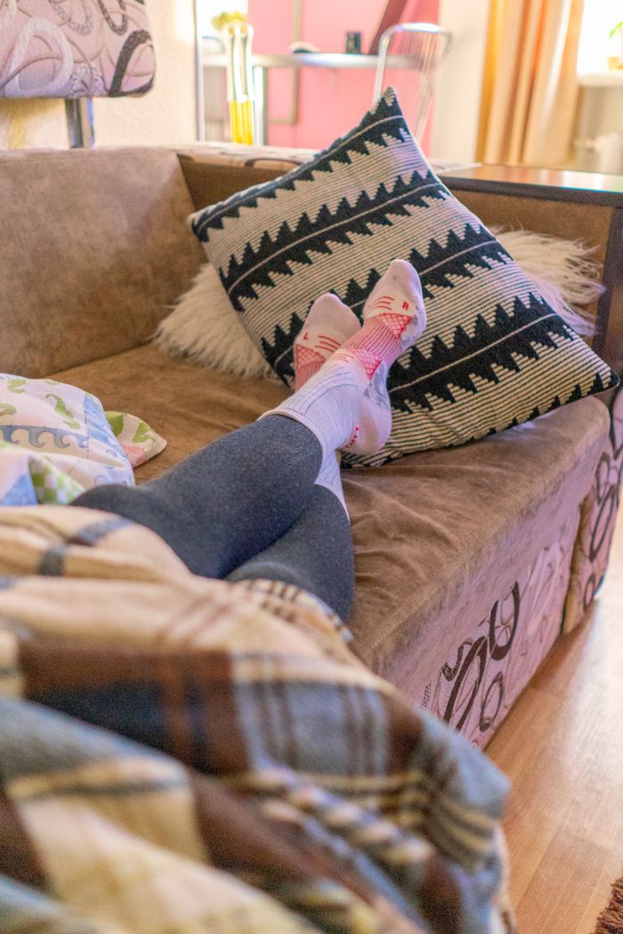 A person relaxing on a sofa with warm socks and a plaid blanket, enjoying a peaceful indoor day.