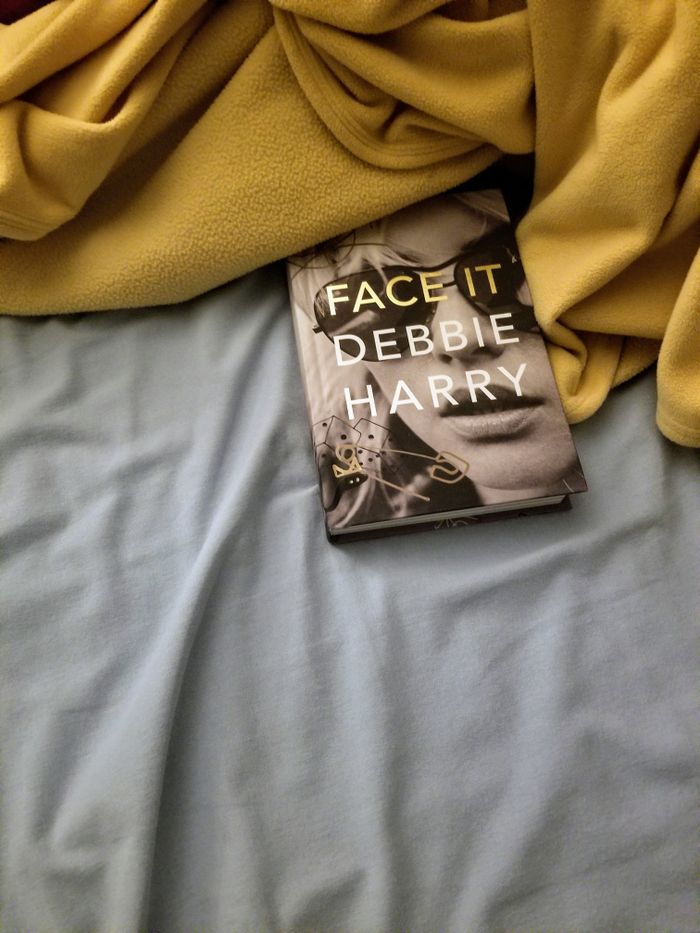 A cozy setup showing the book 'Face It' by Debbie Harry on a bed with soft sheets.