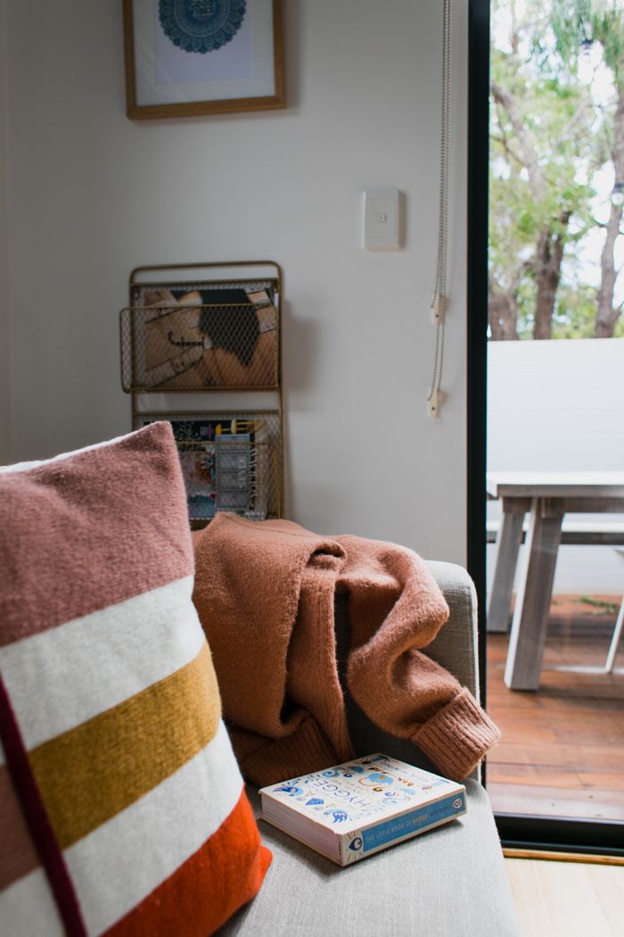 Modern light living room interior with sofa with pillows and book near sweater and entrance in terrace with table