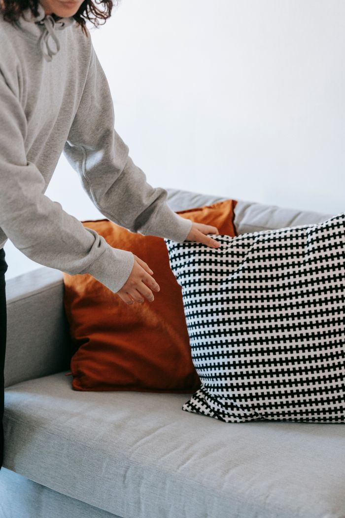 A woman adjusts colorful cushions on a modern couch in a cozy indoor setting.